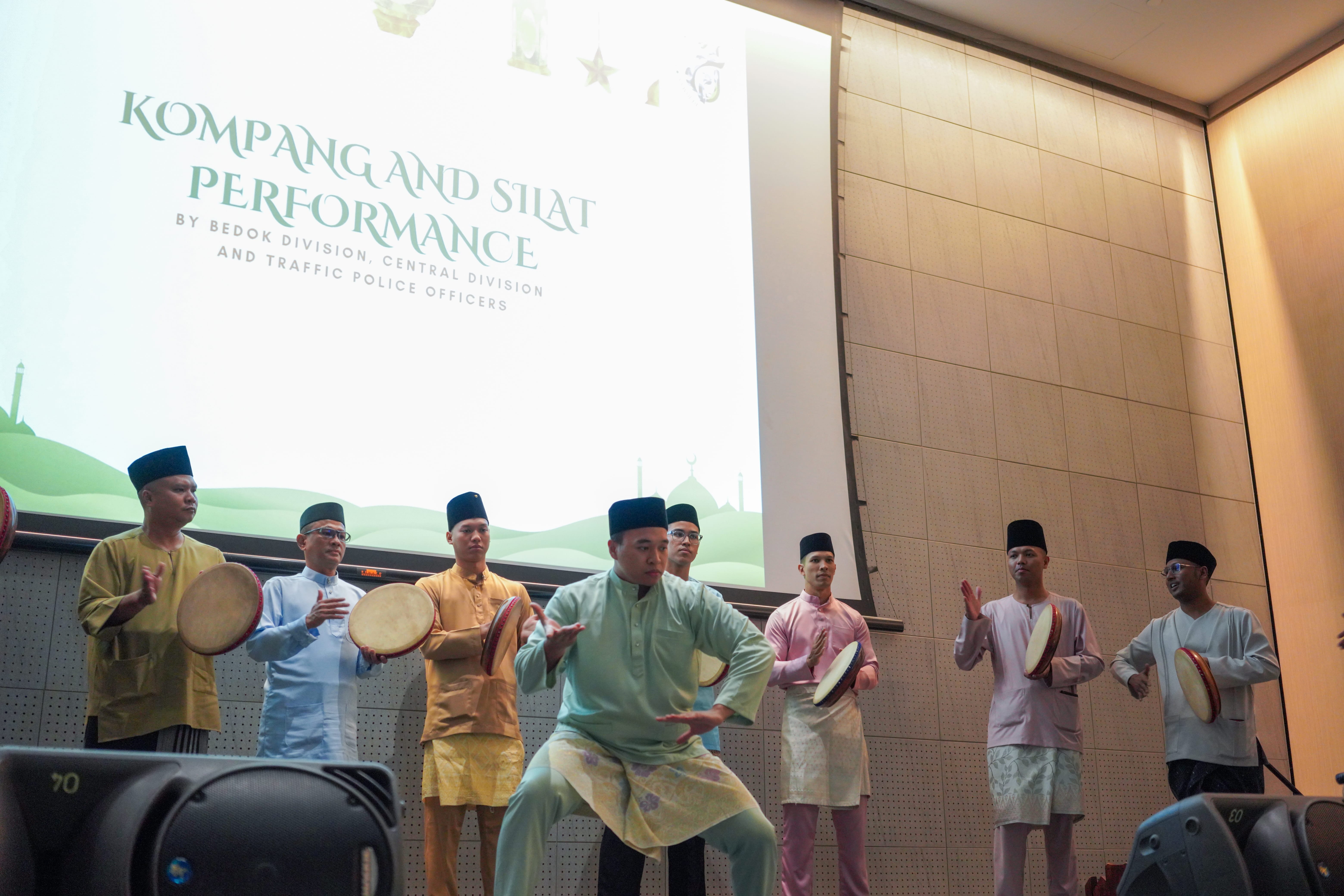 A silat performer demonstrating a martial arts routine on stage while kompang musicians accompany the performance.